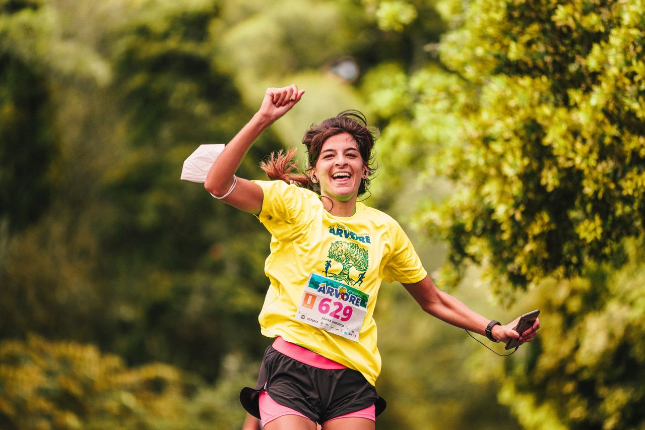 Joyful female runner in yellow participates in an outdoor race amidst lush greenery, embodying athletic enthusiasm.